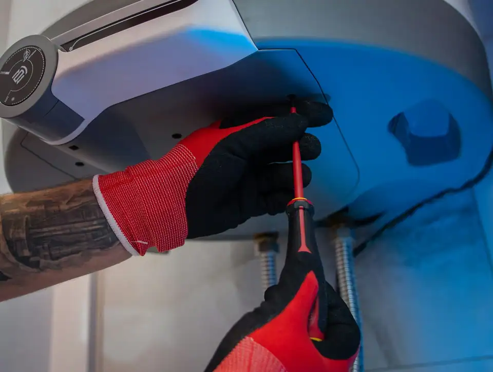 A plumber in red gloves working on a water heater