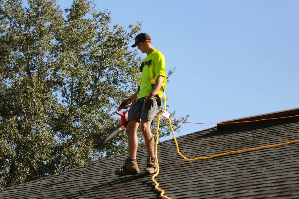 A roofer walking the ridge of a shingle roof with his nail gun